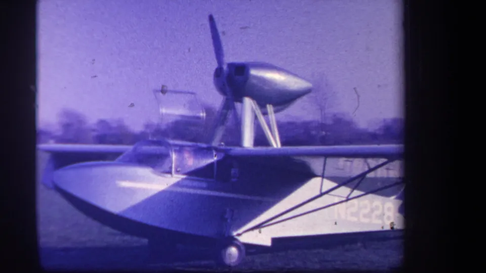 Yucaipa 1959 home-movie frame of a parked amphibious aircraft, showing the canopy, high wing, wheel, and partial N2228 marking.