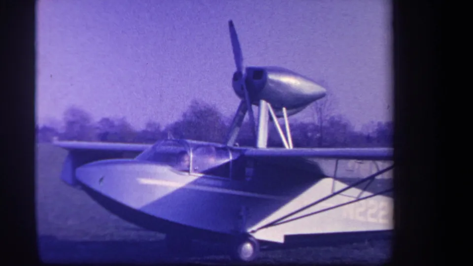 Final 1959 home-movie frame of the stationary amphibious aircraft in Yucaipa, with high wing, canopy, struts, and propeller visible.