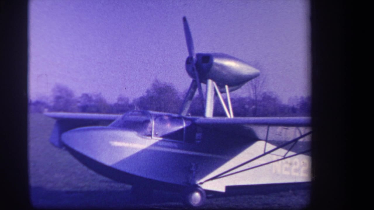 1959 Yucaipa, California 8mm frame showing a silver amphibious aircraft parked on grass with its nose propeller still visible.