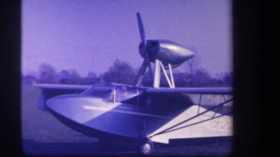 1959 Yucaipa, California 8mm frame showing a silver amphibious aircraft parked on grass with its nose propeller still visible.