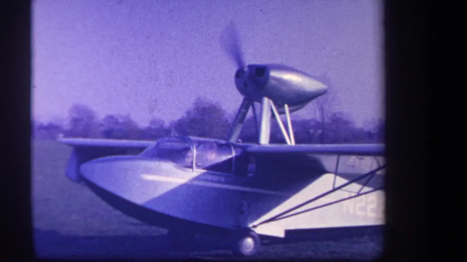 1959 Yucaipa frame showing the amphibious aircraft with its nose propeller spinning rapidly against a rural field backdrop.