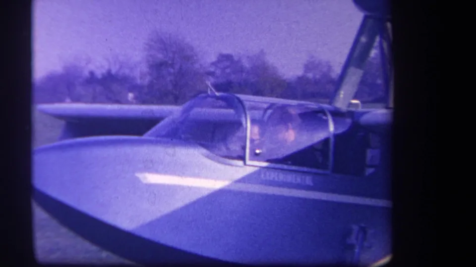 Close 8mm frame from the 1959 Yucaipa clip showing the cockpit canopy, wing surface, side marking, and upper strut structure.