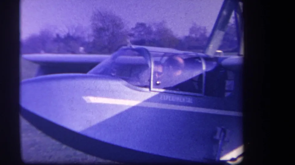 1959 home-movie frame of a small experimental aircraft cockpit at Volmer Yucaipa, with occupants visible through the canopy.