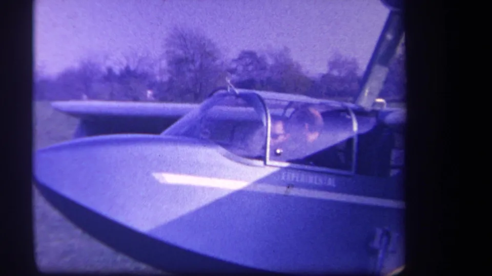 1959 Yucaipa-area 8mm frame showing the aircraft nose, transparent canopy, pilot, and EXPERIMENTAL marking in a blue-purple film cast.