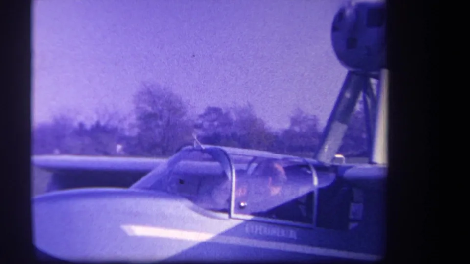 1959 Yucaipa-area home-movie frame showing a person seated in a small aircraft cockpit on a grassy field.