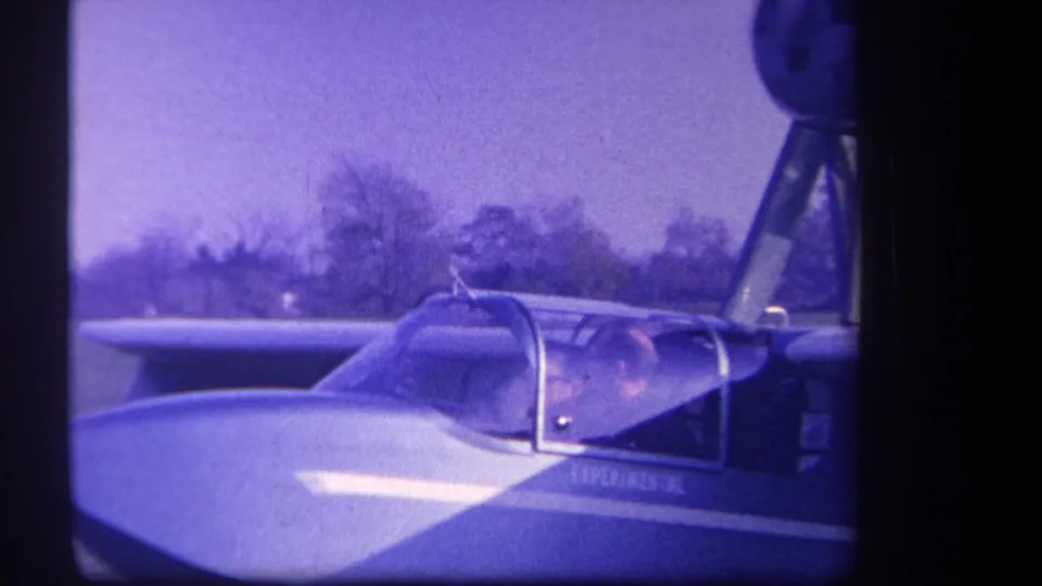 1959 Yucaipa-area frame of a seated cockpit occupant in a small experimental-looking aircraft on grass.