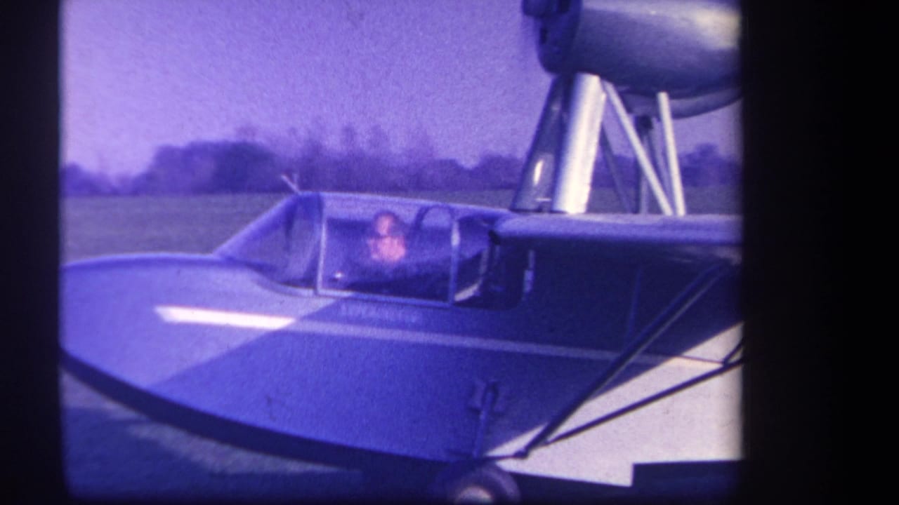1959 Volmer Yucaipa home-movie frame showing a small blue and white aircraft with a seated pilot visible through the cockpit canopy.