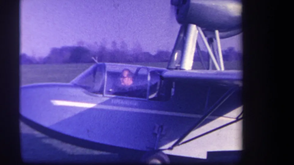 1959 Volmer Yucaipa home-movie frame showing a small blue and white aircraft with a seated pilot visible through the cockpit canopy.