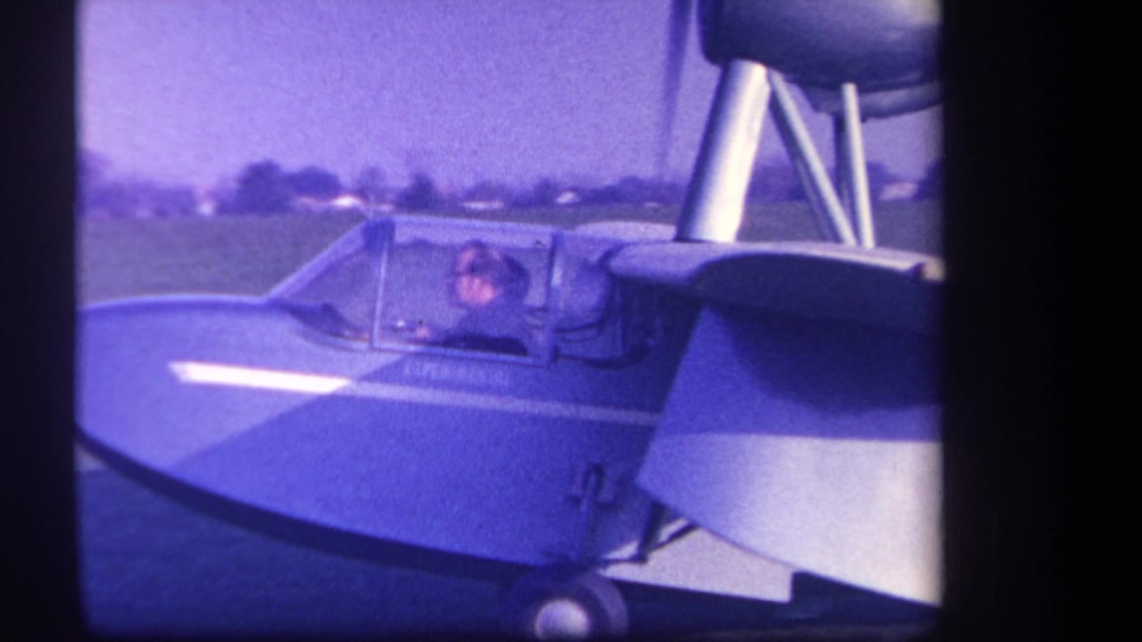 Pilot in the cockpit of a small aircraft seen beside the wing and struts.
