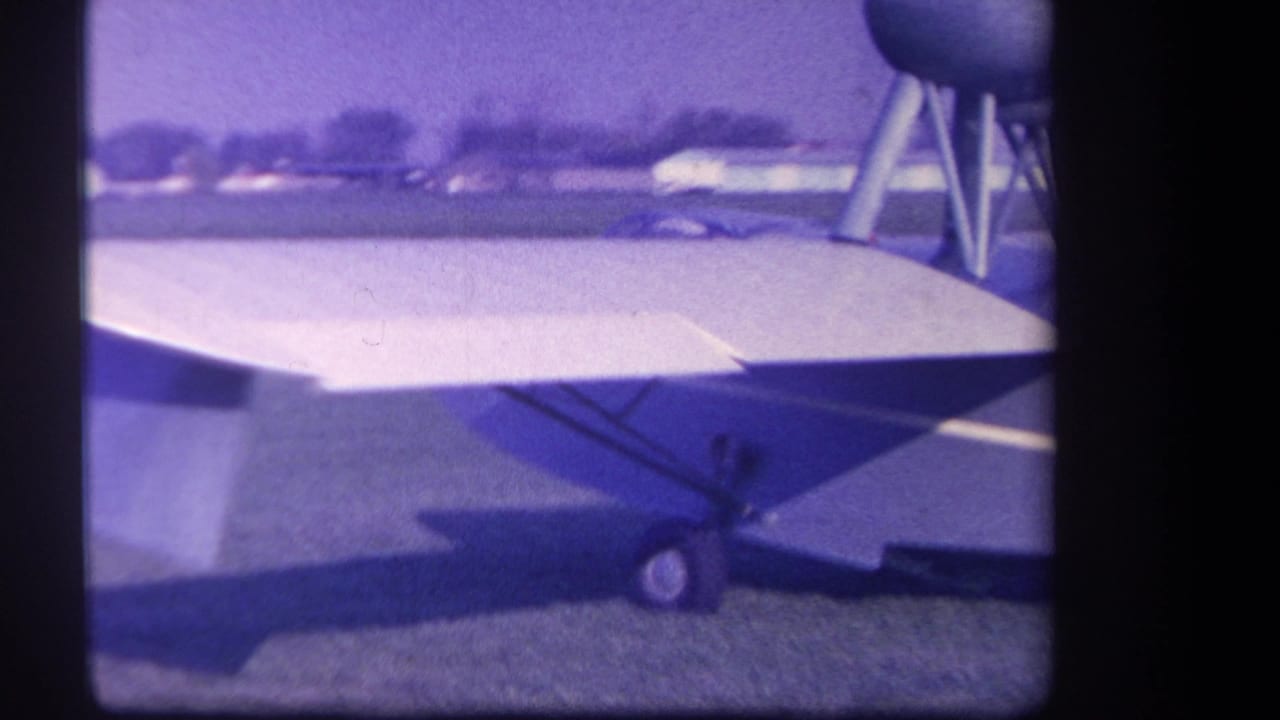 Close side view of a small high-wing airplane on grass with landing gear visible.
