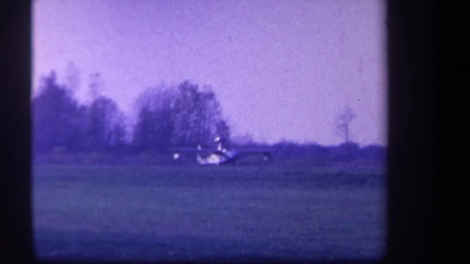 The airplane appears farther across the grass field, framed by trees and open sky in the 1959 home-movie footage.