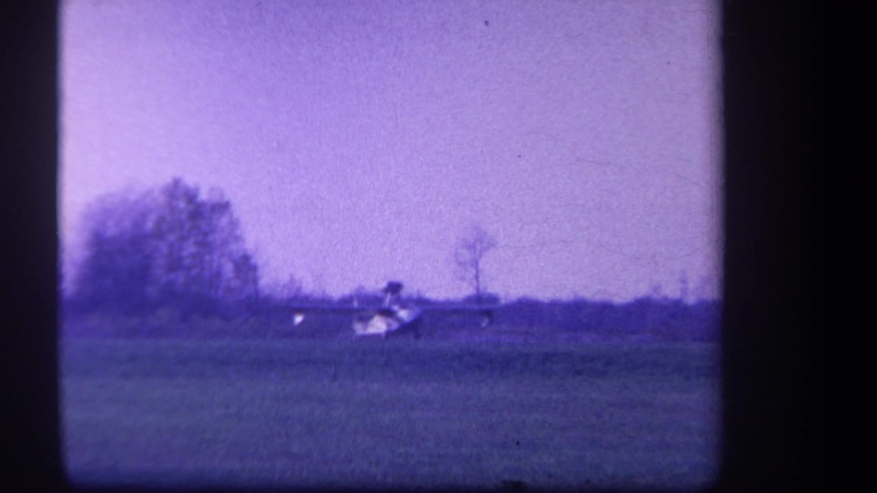 Small light plane on a grassy field with trees along the horizon.