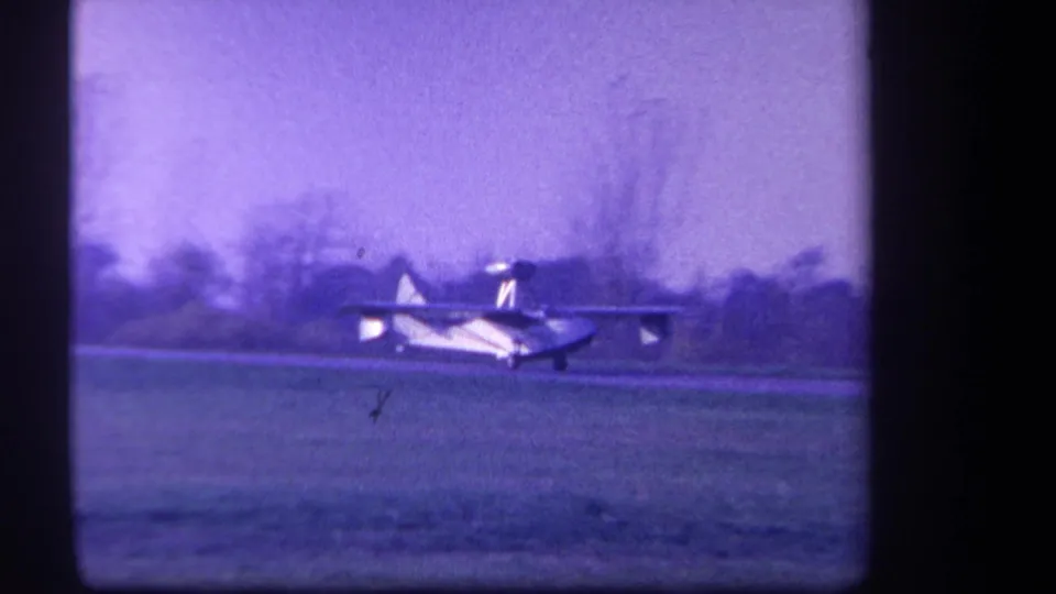 Pontoon-equipped light aircraft crosses a grassy Yucaipa field in a purple-tinted 1959 8mm home-movie frame.