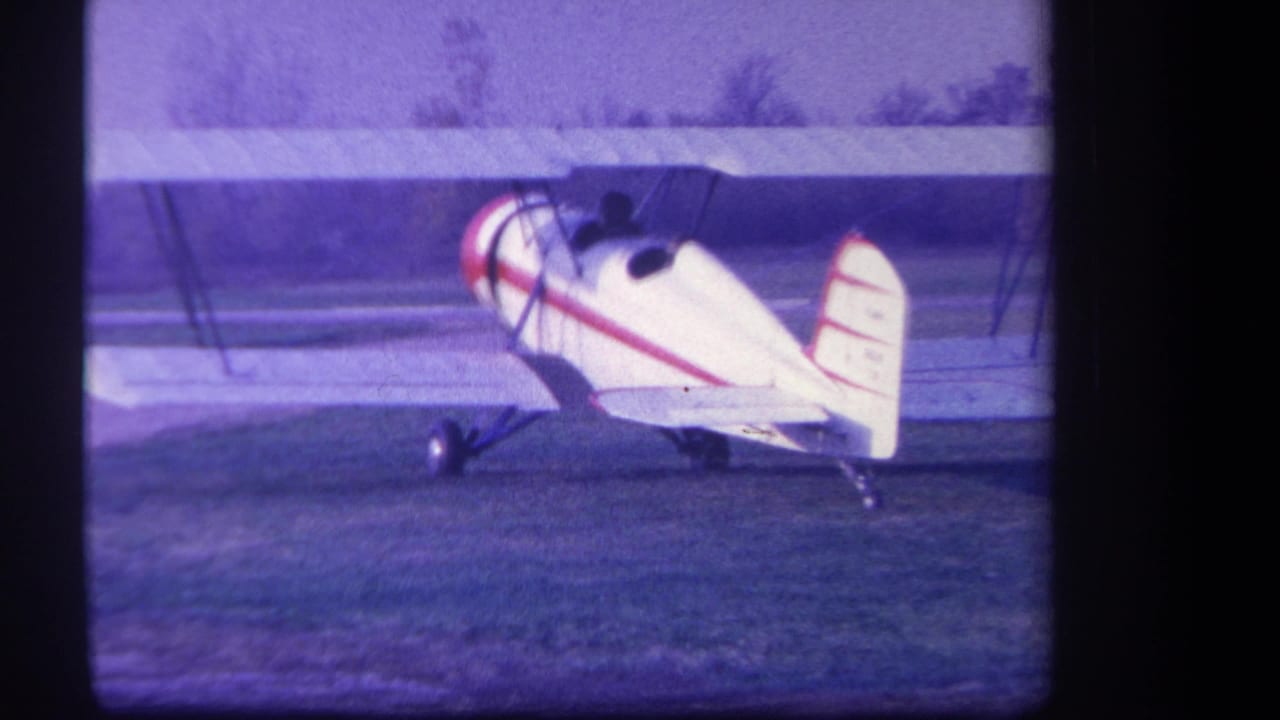 White biplane seen from the side and rear on a grassy airfield.