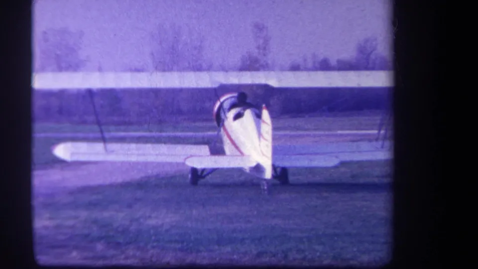 Rear view of the vintage biplane on the Yucaipa airfield, with its wings extending across the purple-tinted frame.