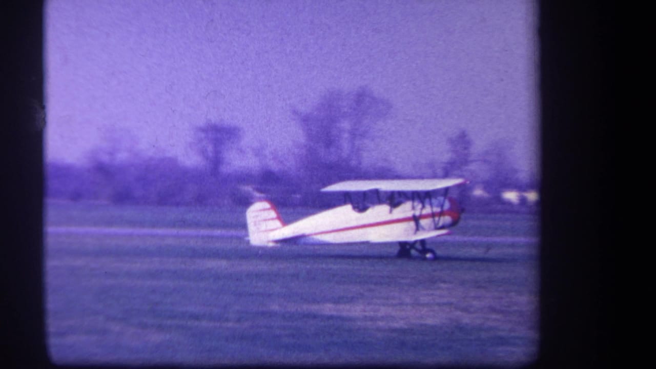 The biplane taxis across the Yucaipa grass airfield, with seated people visible in the open cockpit area.