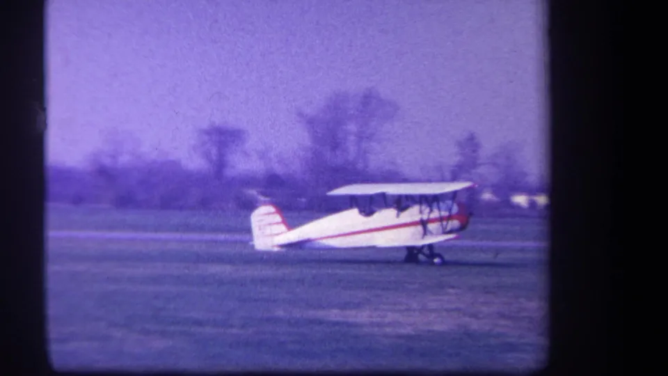 The biplane taxis across the Yucaipa grass airfield, with seated people visible in the open cockpit area.