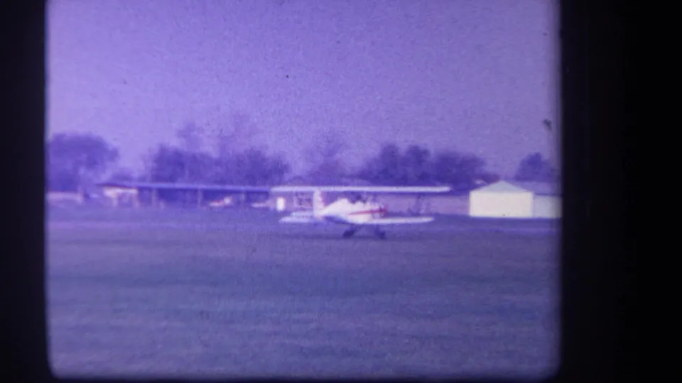 1959 Yucaipa-area 8mm frame showing the biplane smaller in the frame, taxiing near low buildings and trees.