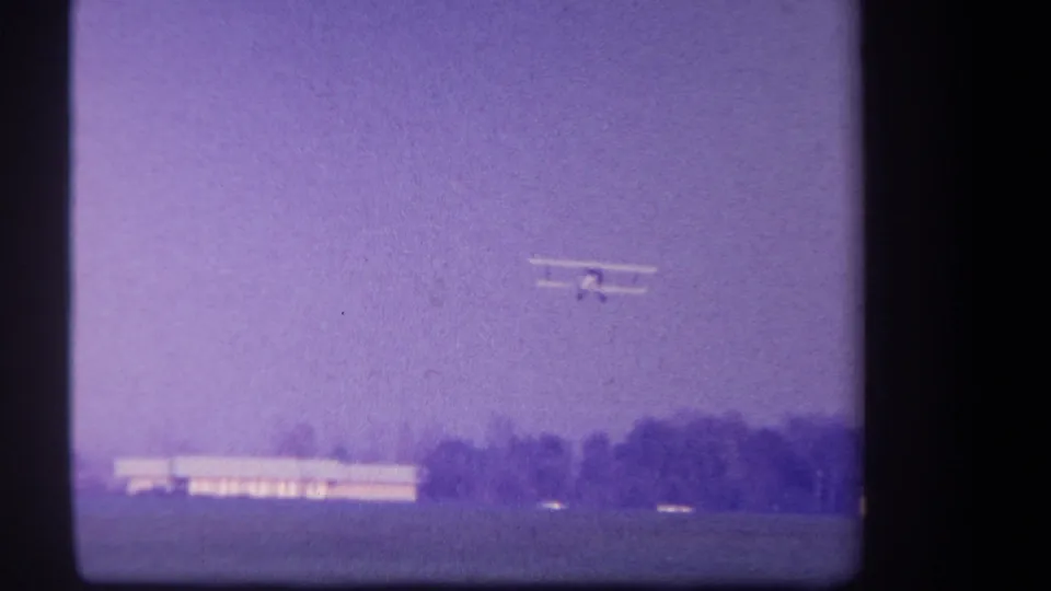 A small biplane appears in the purple-tinted sky over rural Volmer Yucaipa, California, in 1959 home-movie footage.