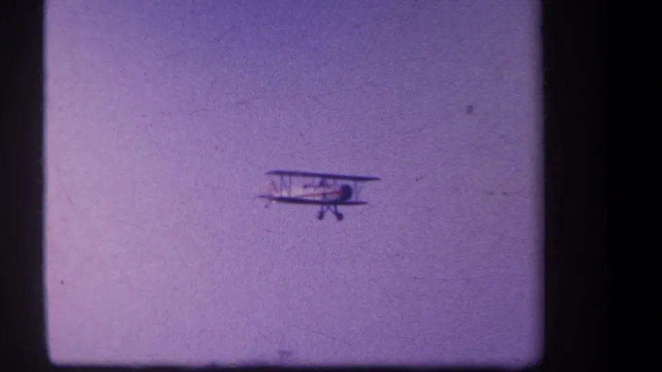 1959 8mm frame of a white and red biplane flying low in the sky near Volmer Yucaipa, California.