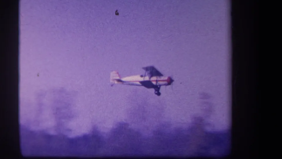 Closer 8mm view of the low-flying biplane against a hazy rural background in Volmer Yucaipa.