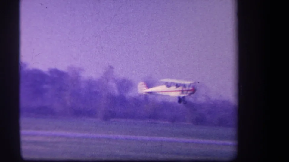 1959 Yucaipa-area home-movie frame showing a small white prop plane low over a grass runway, with trees and a hazy sky behind it.