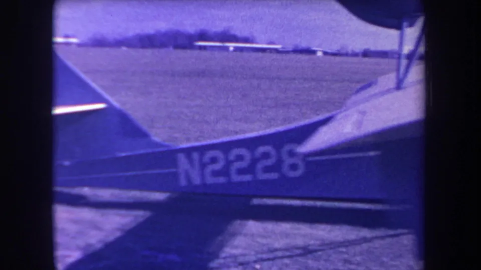 1963 8mm frame from Yucaipa showing the tail section of a small autogyro or aircraft marked N2228 on a grass airfield.