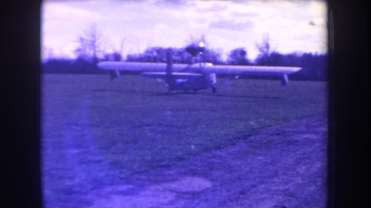 1963 Yucaipa home-movie frame showing a small long-wing propeller aircraft on a grass airstrip under a pale sky.