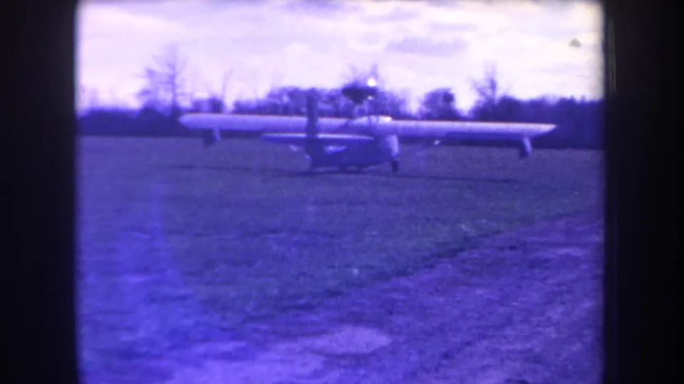 1963 Yucaipa home-movie frame showing a small long-wing propeller aircraft on a grass airstrip under a pale sky.