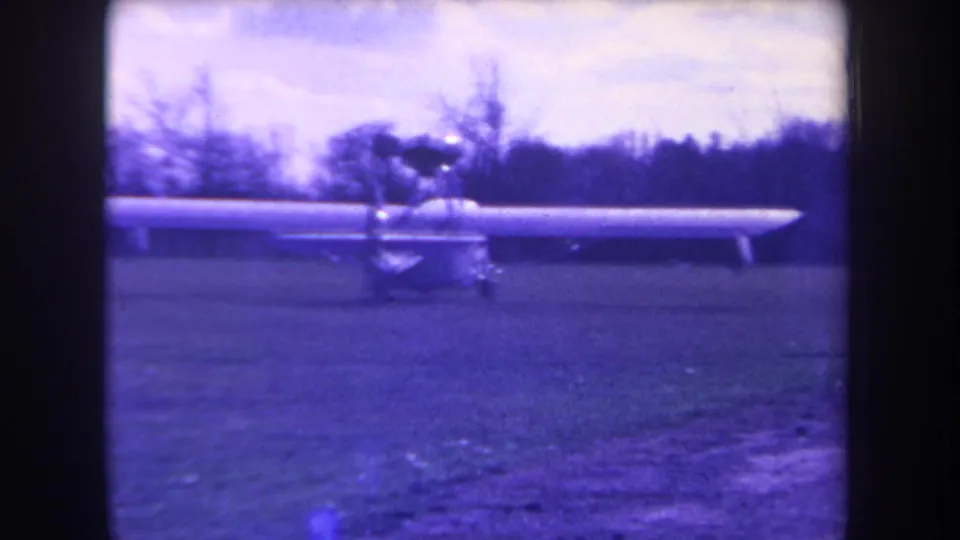 Closer 1963 frame of the small aircraft on a grassy rural airstrip, its long wing spanning most of the view.