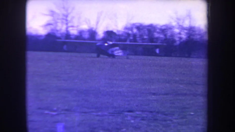 The final 1963 Yucaipa frame shows the small plane from a slight side angle on the grass, with trees and soft aged-film color behind it.