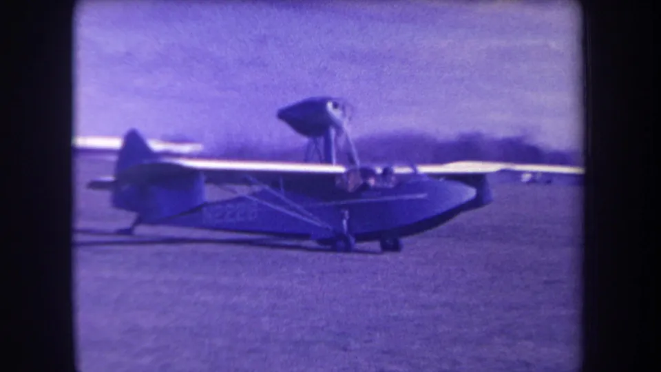 Closer 8mm frame of the small amphibious airplane moving left to right on a grass airfield in Yucaipa.