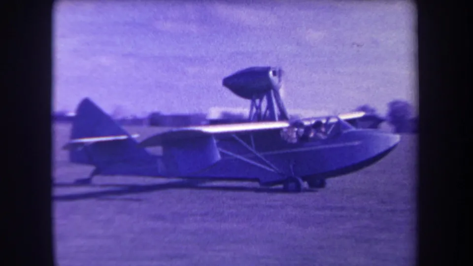 1963 Yucaipa home-movie frame showing a small amphibious aircraft from the side, with people visible in the cockpit and a high-mounted propeller pod.