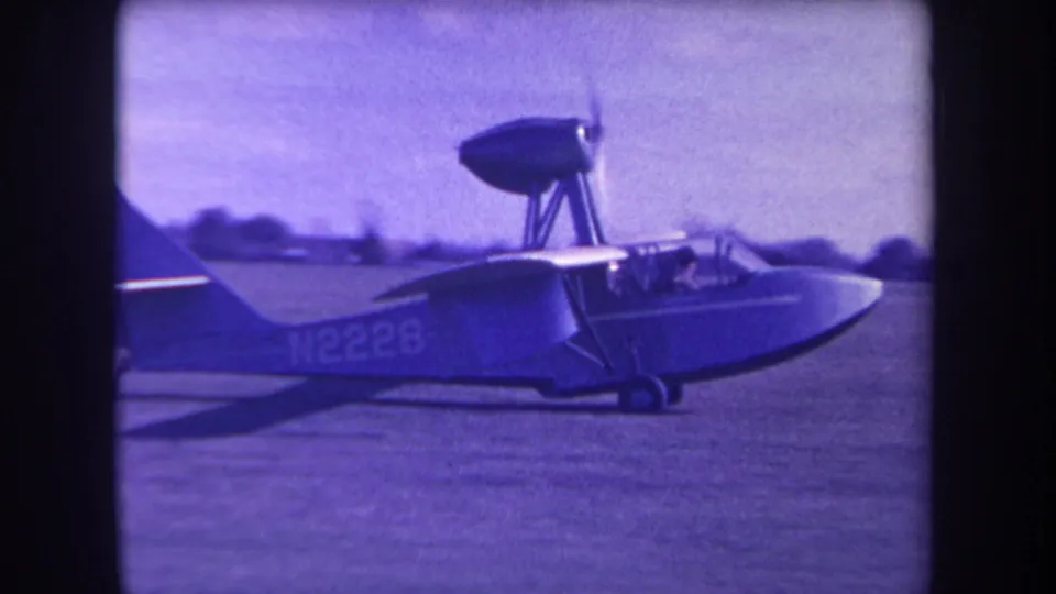 1963 Yucaipa frame showing the amphibious aircraft closer to center, with registration N2228 visible and cockpit figures under soft purple film color.