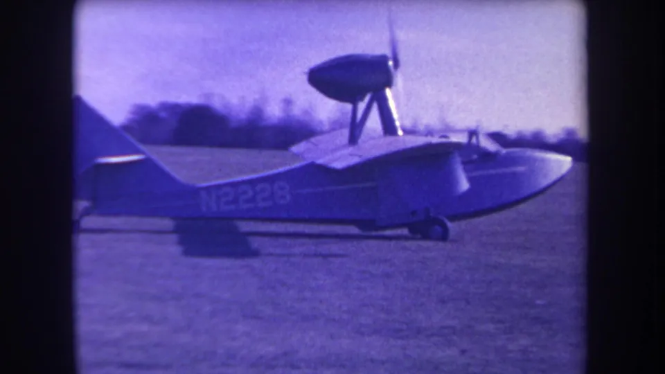 1963 Yucaipa home-movie frame showing the side profile of the small amphibious plane, including tail, wing, cockpit area, and N2228 marking.