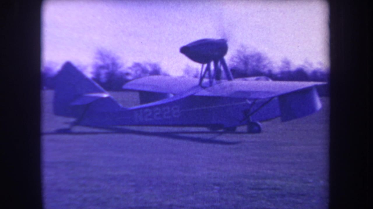 1963 Volmer Yucaipa 8mm frame showing a small single-engine aircraft on grass with a spinning propeller and visible registration markings.