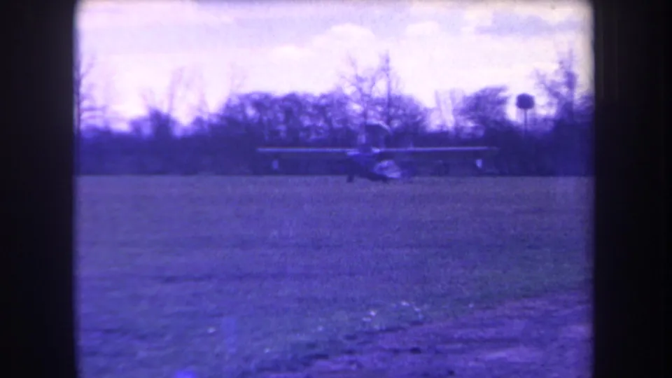 Distant view of the small aircraft moving across the grass at Volmer Yucaipa, California, in purple-tinted 1963 home-movie footage.