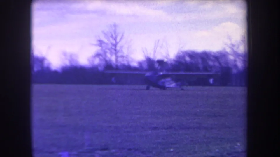 Purple-tinted 8mm view of a small aircraft taxiing across a grassy Yucaipa airfield in 1963.