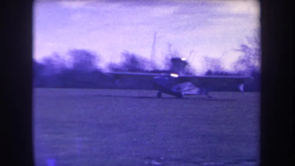 1963 8mm frame showing a small amphibious aircraft moving across grass in California, with a soft purple color cast.