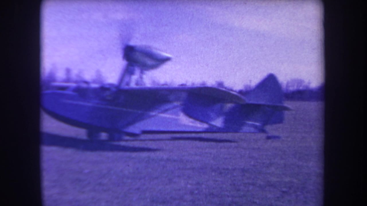 1963 home-movie frame from Yucaipa area showing a small amphibious aircraft parked on grass with soft focus and purple color cast.