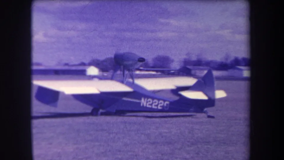 Small aircraft in Volmer Yucaipa, California, seen side-on in aged 8mm color with its upper propeller assembly visible.