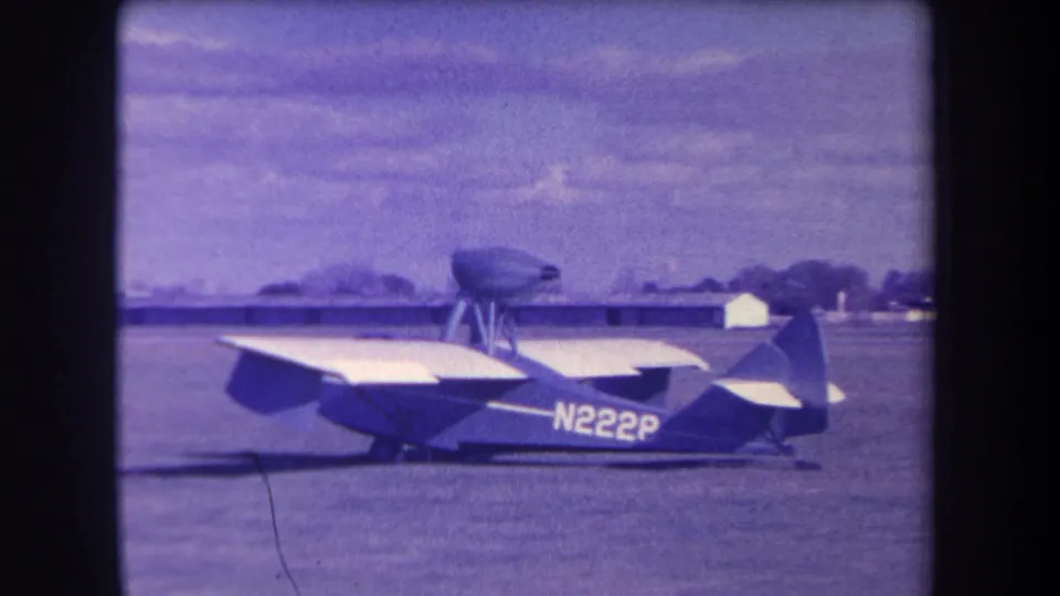 1963 home-movie frame showing the small N2228 aircraft from a side angle on a grassy airfield under clouds.