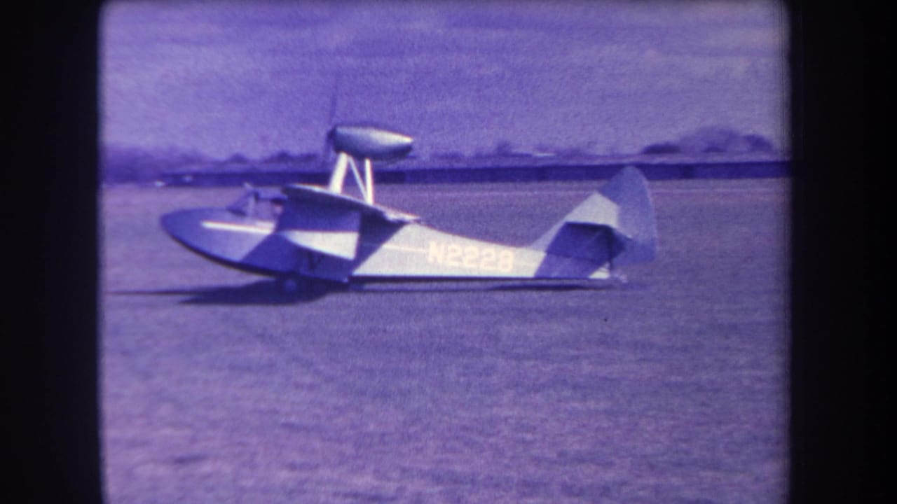 1963 home-movie frame showing a Volmer Yucaipa amphibious aircraft in side profile on a grassy airfield in California.
