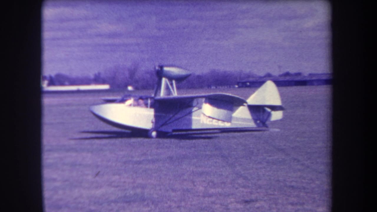 Amphibious plane seen from the side on grass, with a small figure near the cockpit area.