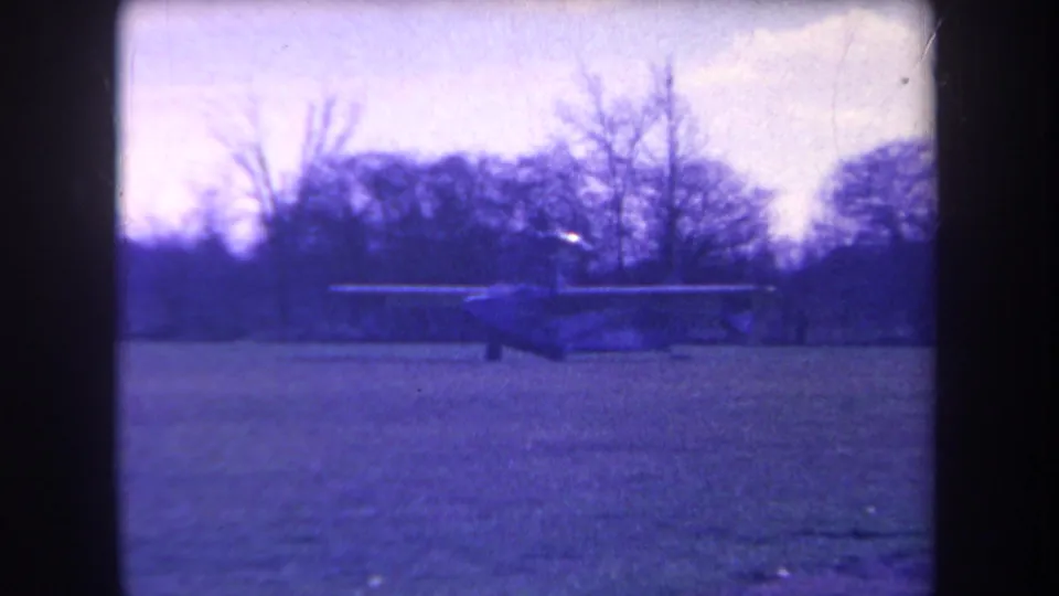 Wide 1963 Yucaipa airfield view with the small aircraft seen in silhouette against trees and open grass.