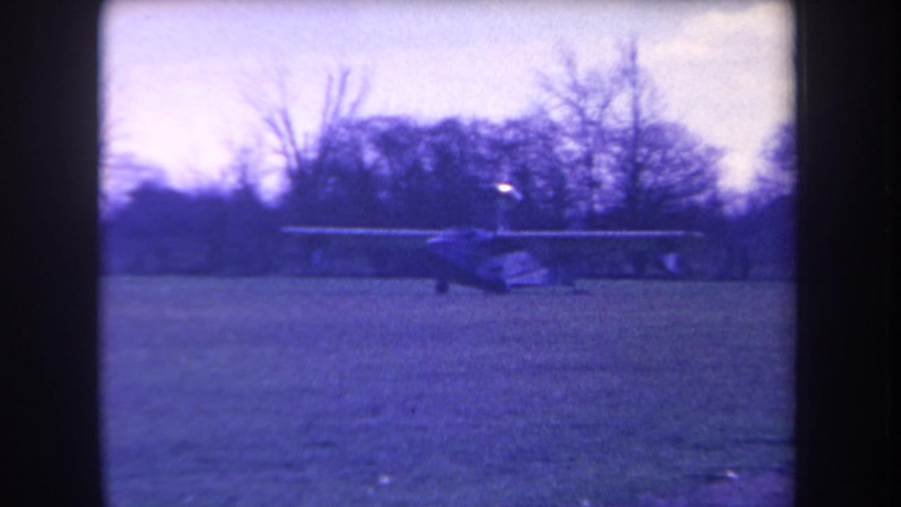 1963 home-movie frame from Volmer Yucaipa showing a small light plane on grass with bare trees and a blue color cast.