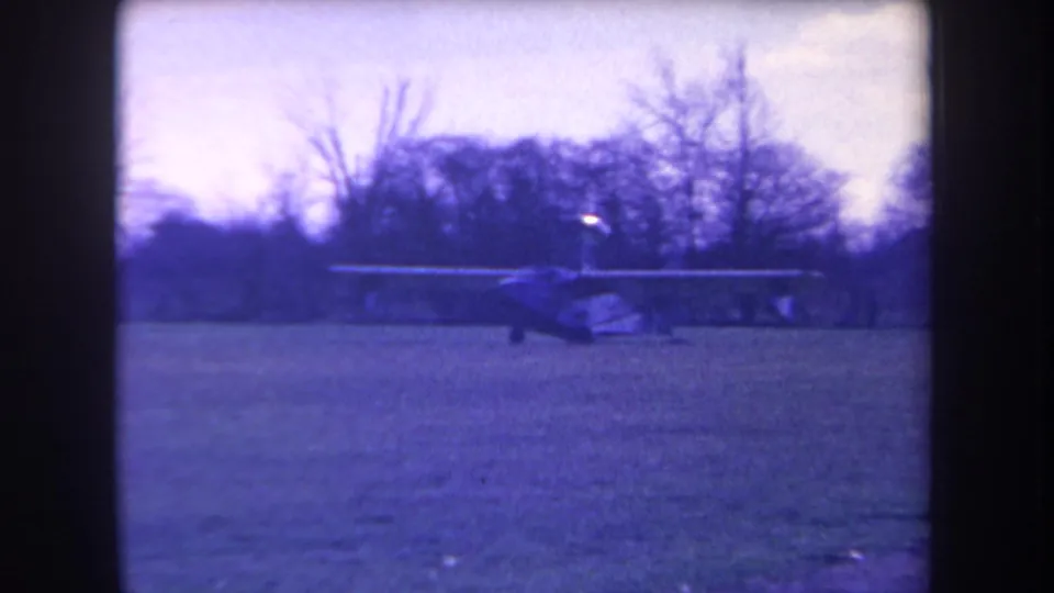 1963 home-movie frame from Volmer Yucaipa showing a small light plane on grass with bare trees and a blue color cast.