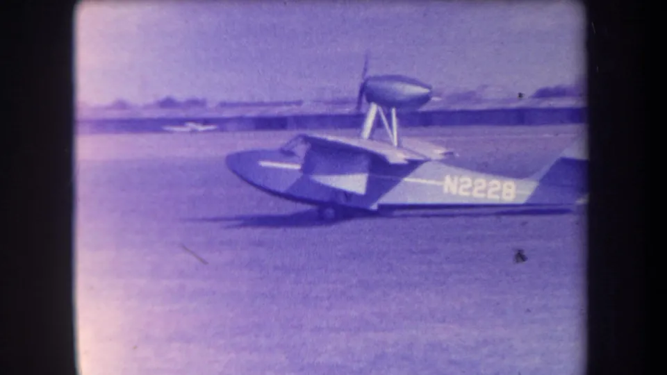 Final 1963 home-movie frame from Yucaipa showing the N2226 aircraft side-on, with grass field, tail, wing, and elevated dish-like structure visible.