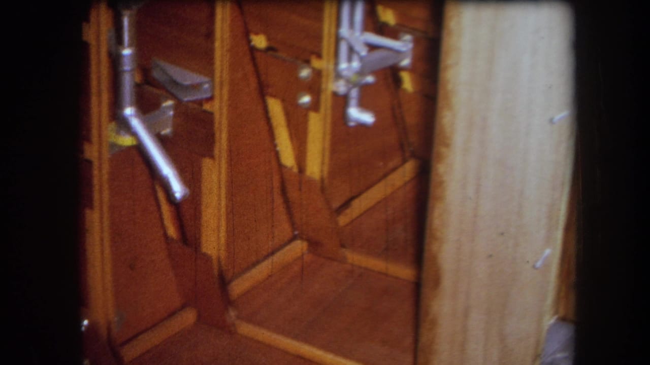 Close view of a wooden mechanical interior with metal rods, brackets, fasteners, and a pale vertical board.