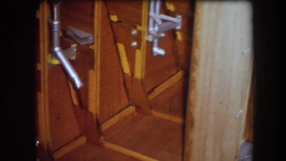 1964 8mm frame from the Yucaipa-area reel showing varnished wood panels, angled braces, metal rods, and hardware inside a mechanism.